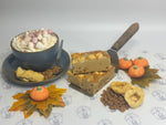 Dessert platter with a bowl of hot chocolate, slices of cake, and decorative pumpkins on a patterned tablecloth.